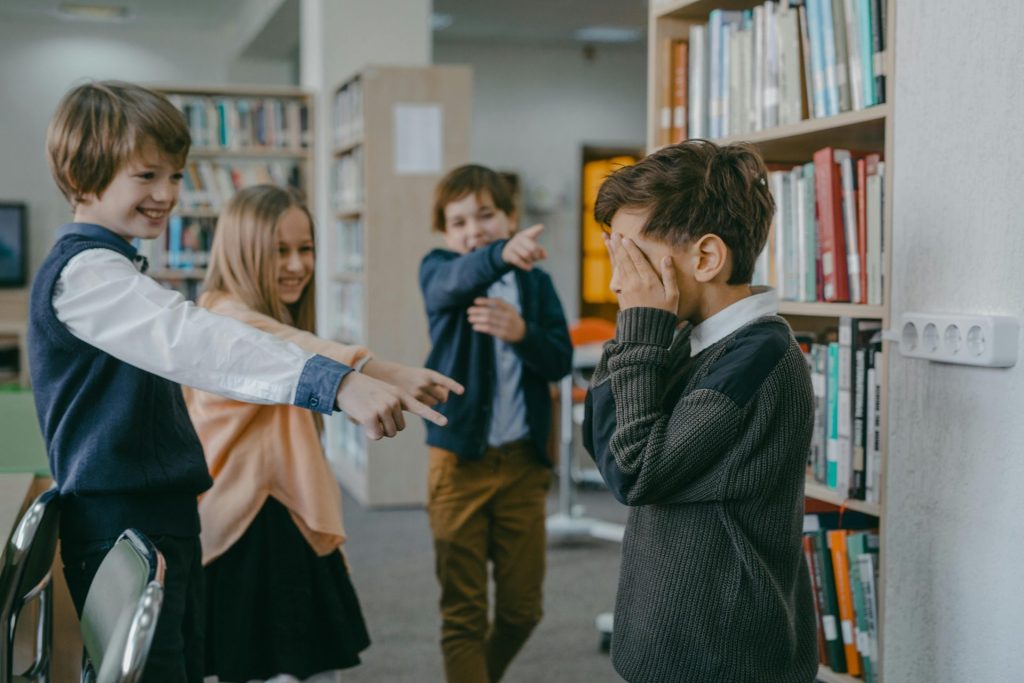 Eine Gruppe von Kindern schikaniert einen Klassenkameraden in einer Schulbibliothek.