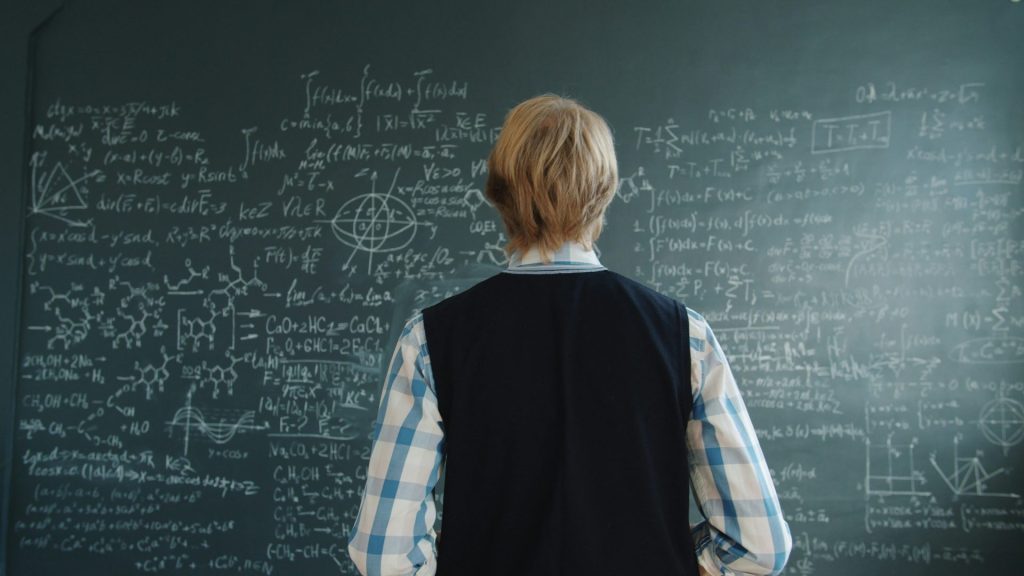 Student looking at complex mathematical formulas on blackboard.